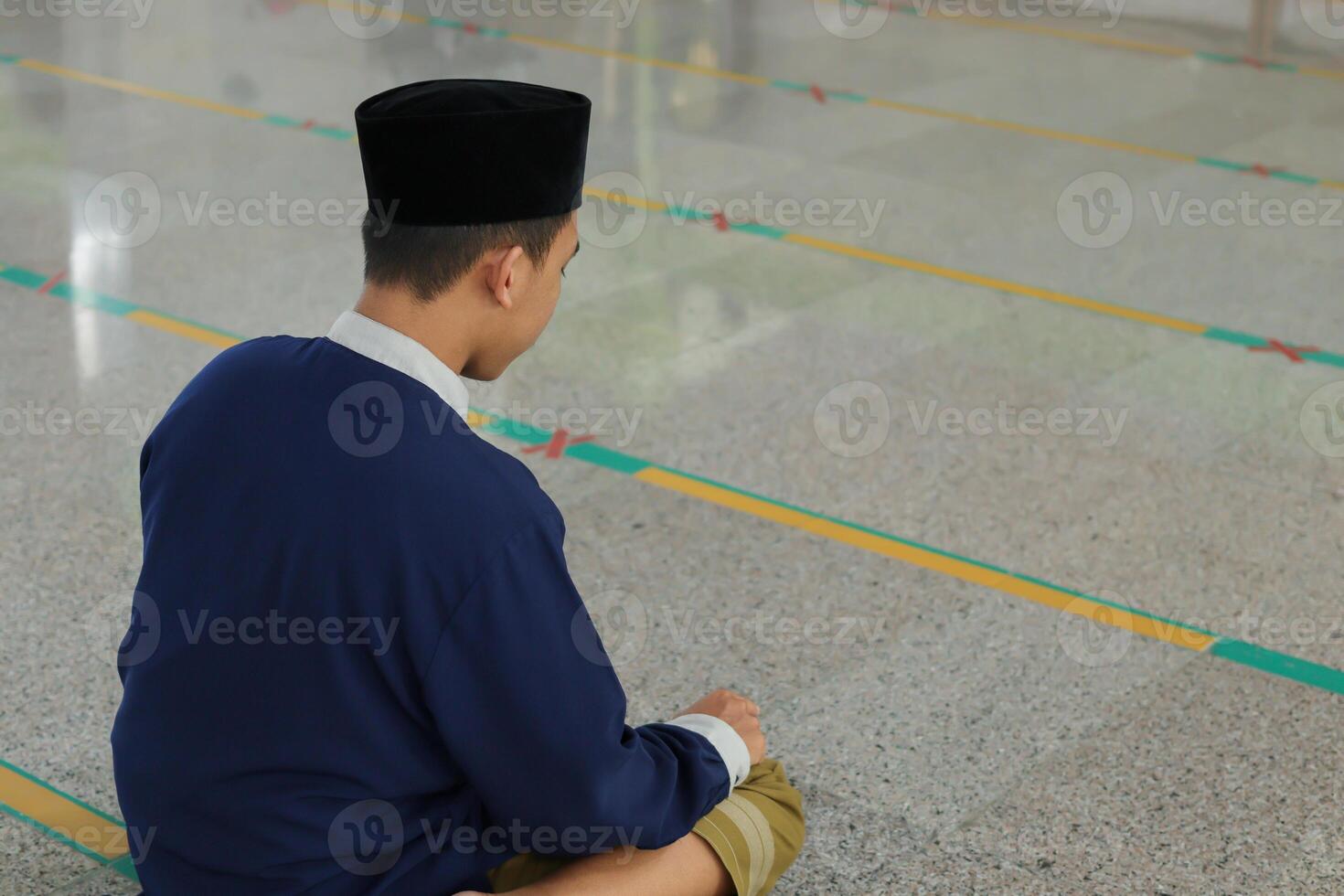 Portrait of religious Asian man in muslim shirt praying and doing salat or sholat in mosque photo