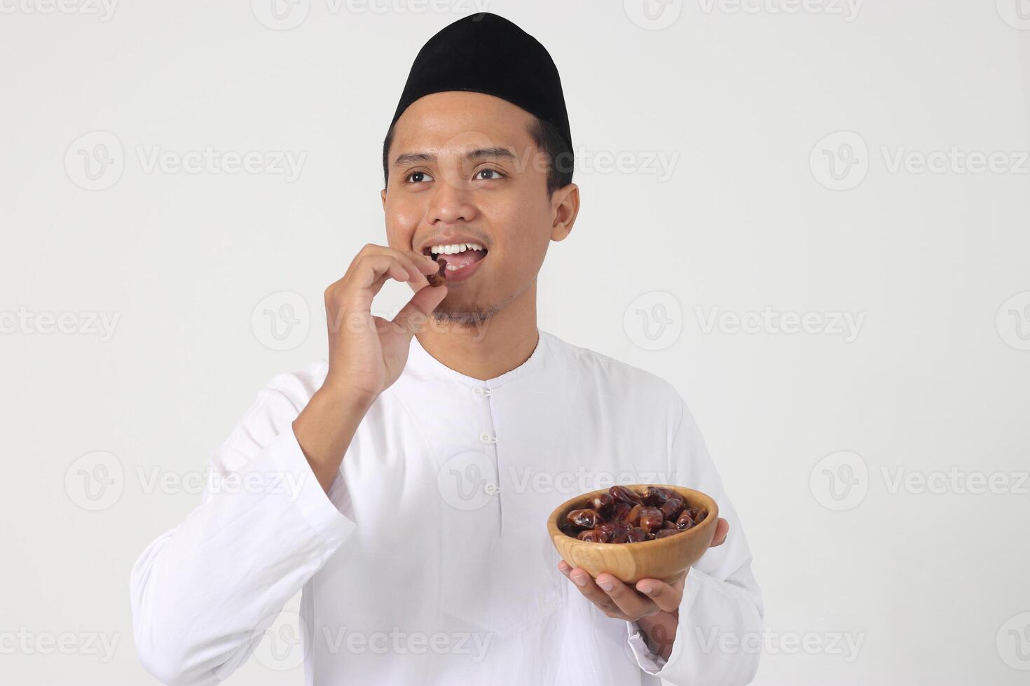 Portrait of excited Asian muslim man eating date fruit during sahur or breaking the fast. Culture and tradition on Ramadan month. Isolated image on white background photo