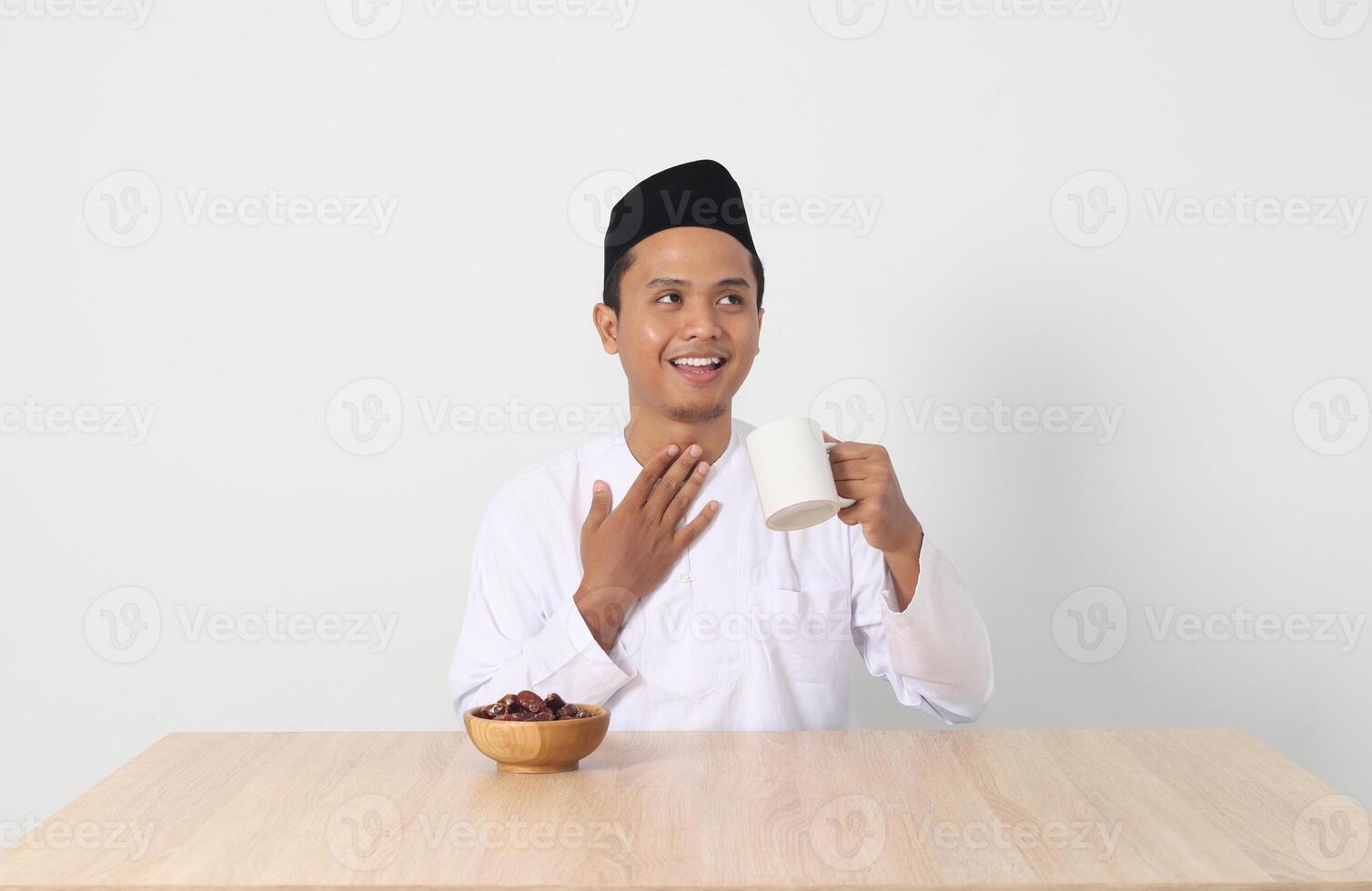 Portrait of serious Asian muslim man drinking a glass of water during sahur and breaking fast. Culture and tradition on Ramadan month. Isolated image on white background photo