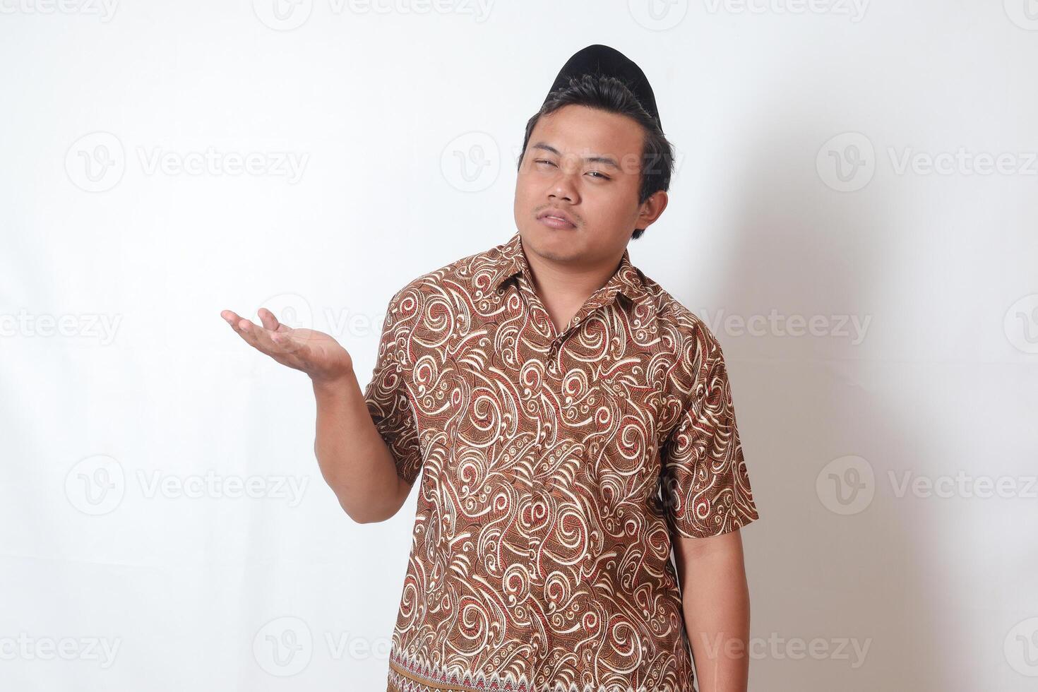 retrato de confuso asiático hombre vistiendo batik camisa y Songkok demostración vacío mano. aislado imagen en gris antecedentes foto
