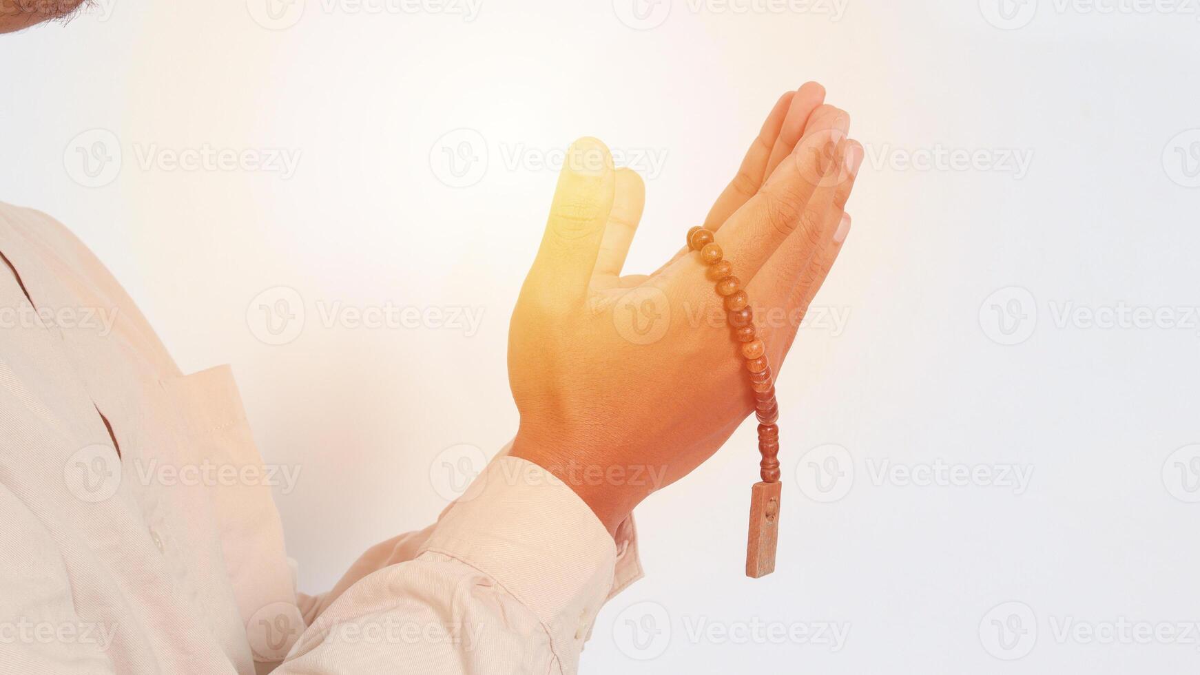 Close up hand of religious Asian muslim man in koko shirt with skullcap praying earnestly with his hands raised, holding islamic beads. Devout faith concept. Isolated image on white background photo