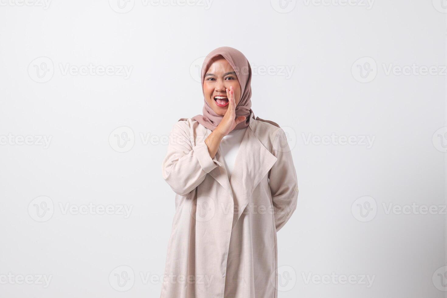 Portrait of excited Asian hijab woman in casual suit screaming announcement and whispering gossip. Businesswoman concept. Isolated image on white background photo