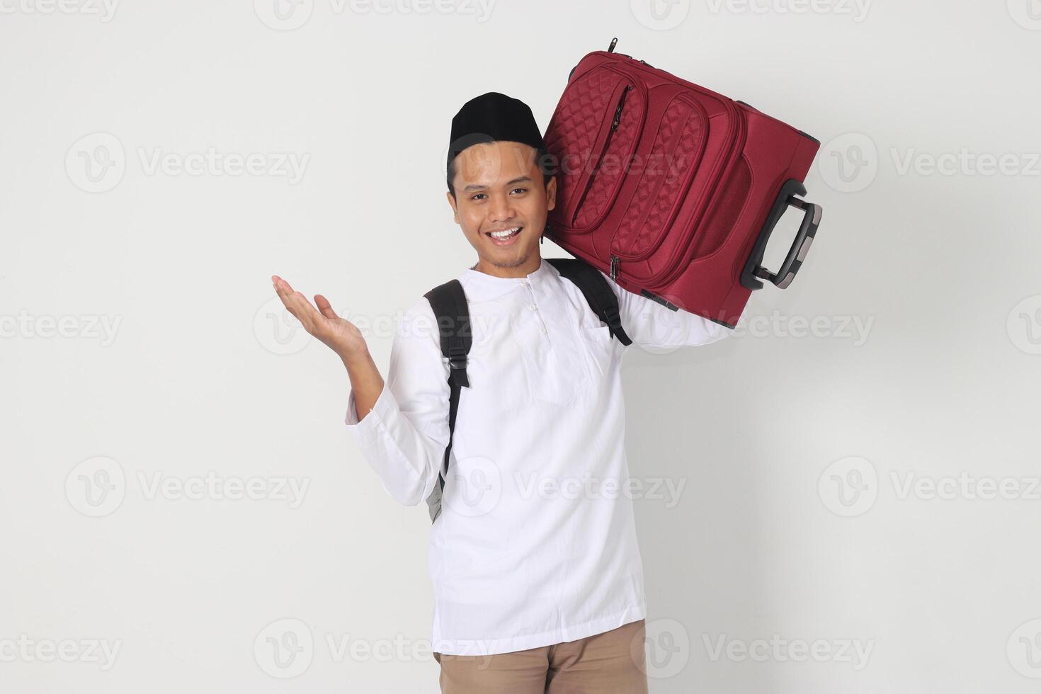 Portrait of excited Asian muslim man carrying suitcase pointing with hand to the side. Going home for Eid Mubarak. Isolated image on white background photo