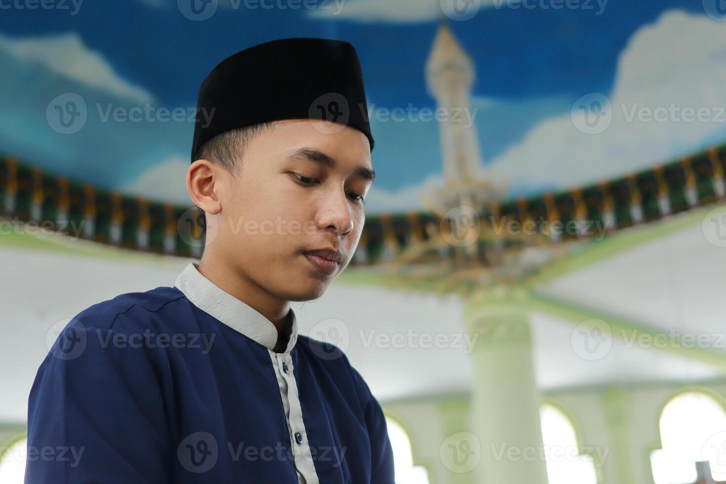 Portrait of religious Asian man in muslim shirt praying and doing salat or sholat in mosque photo