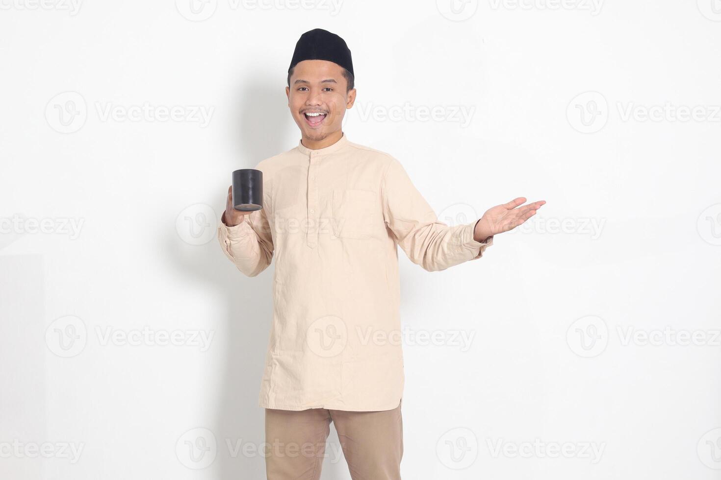 Portrait of attractive Asian muslim man in koko shirt with peci holding a mug, drinking water, quenching thirst after fasting. Isolated image on white background photo