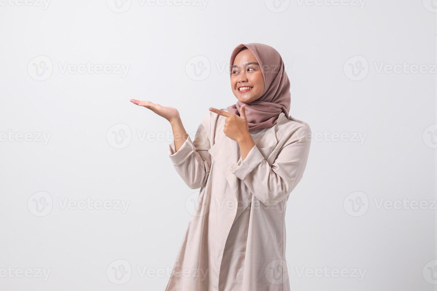 retrato de emocionado asiático hijab mujer en casual traje señalando y demostración producto en su lado con dedo. mujer de negocios concepto. aislado imagen en blanco antecedentes foto