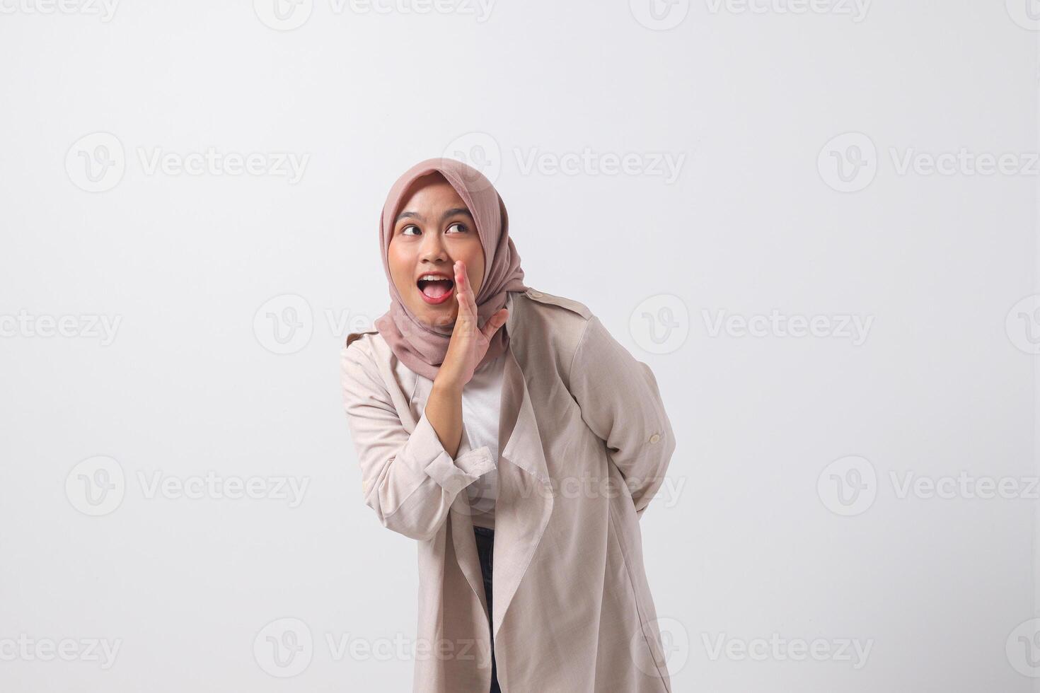 Portrait of excited Asian hijab woman in casual suit screaming announcement and whispering gossip. Businesswoman concept. Isolated image on white background photo