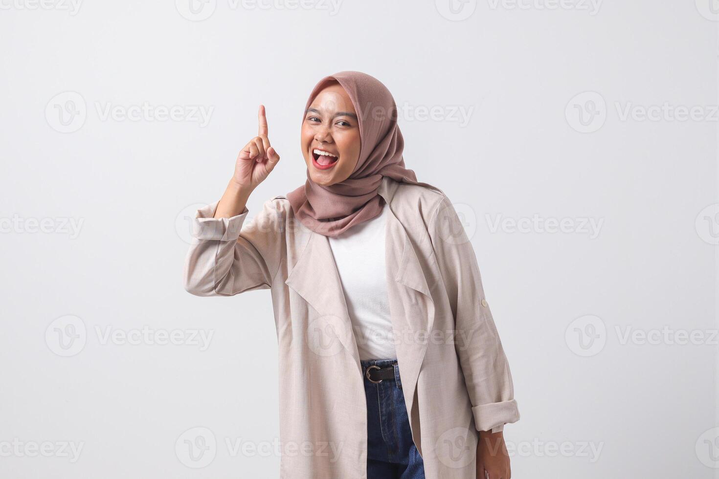 Portrait of excited Asian hijab woman in casual suit pointing up her forefinger and reminding something to do. Businesswoman concept. Isolated image on white background photo