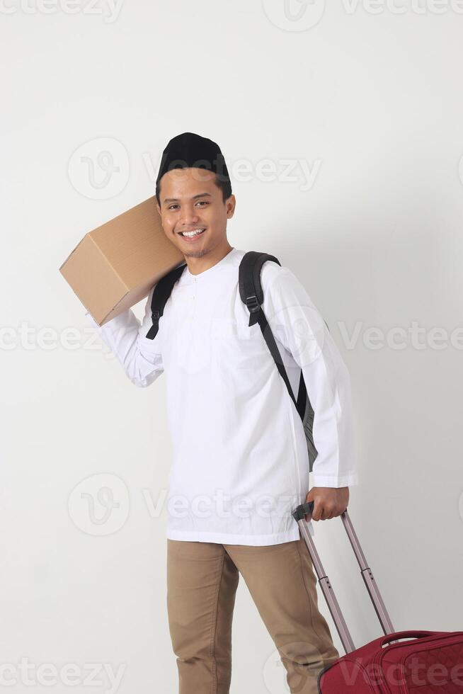Portrait of attractive Asian muslim man carrying cardboard box and suitcase and standing with confident. Going home for Eid Mubarak. Isolated image on white background photo