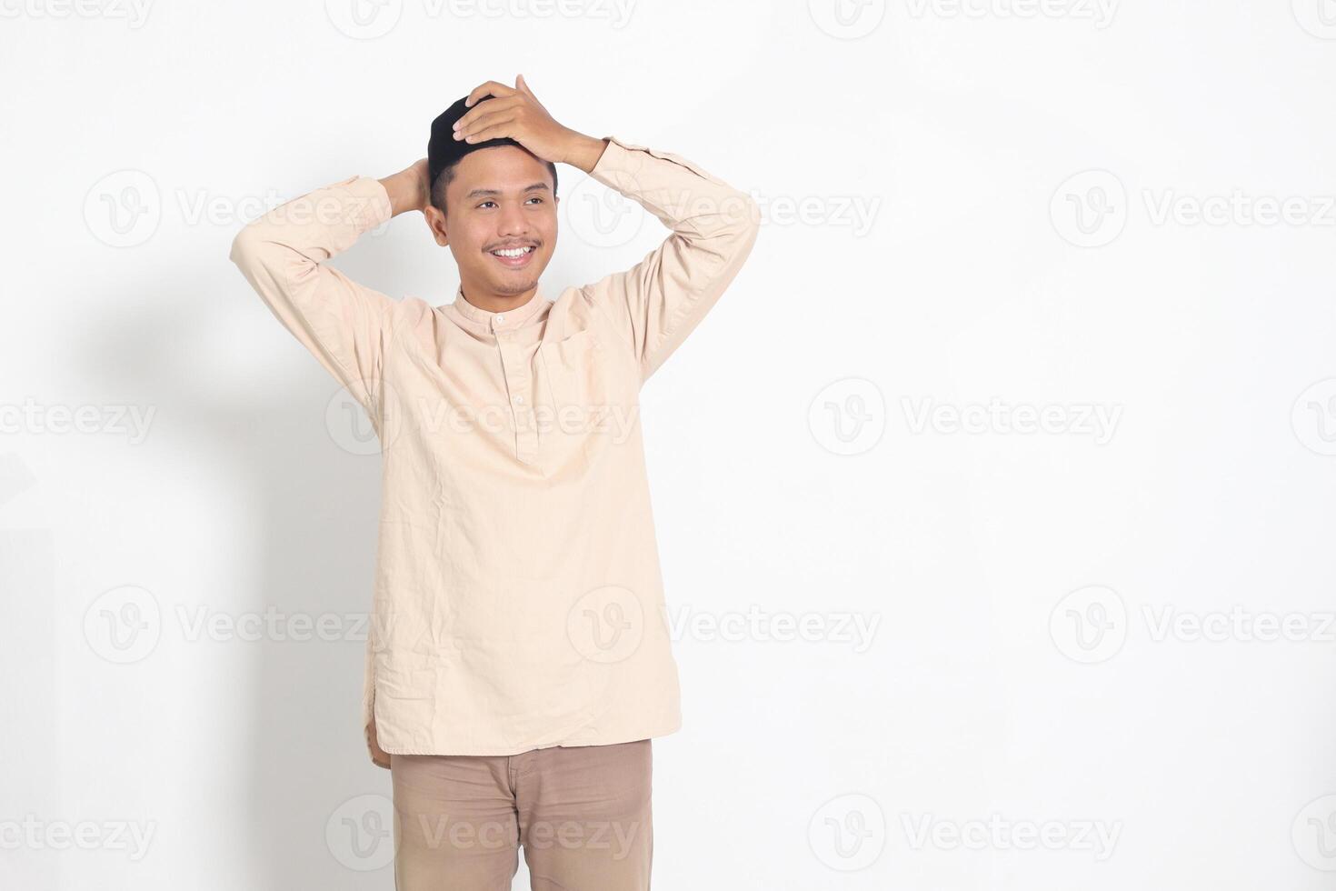 Portrait of excited Asian muslim man in koko shirt trying to adjust his songkok or peci or black skullcap. Isolated image on white background photo