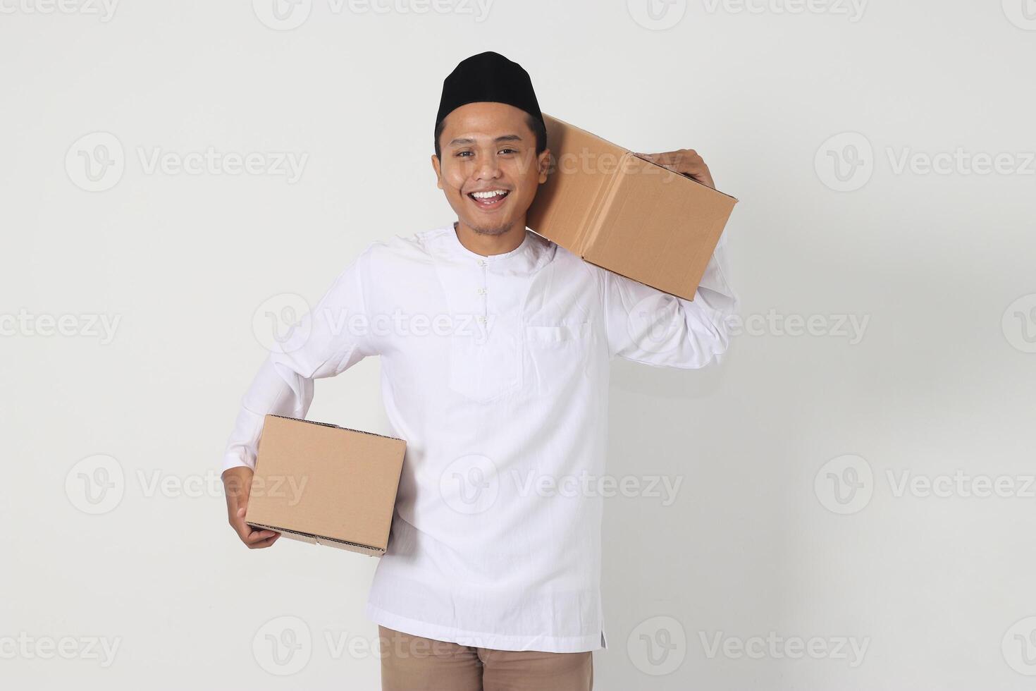 Portrait of happy excited Asian muslim man going home for Eid Mubarak. Indonesian guy carrying cardboard box. Isolated image on white background photo