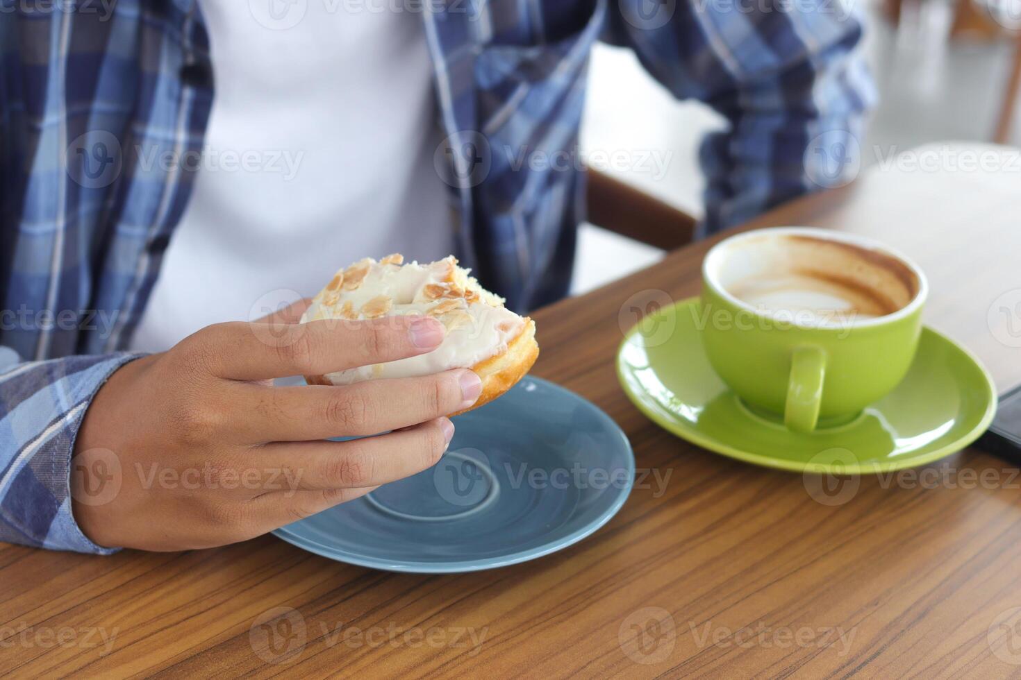 Close up of male hand eating sweet donut in cafe photo