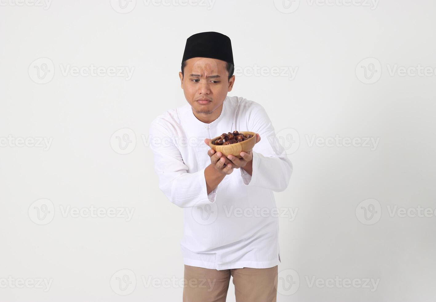 Portrait of excited Asian muslim man eating date fruit during sahur or breaking the fast. Culture and tradition on Ramadan month. Isolated image on white background photo