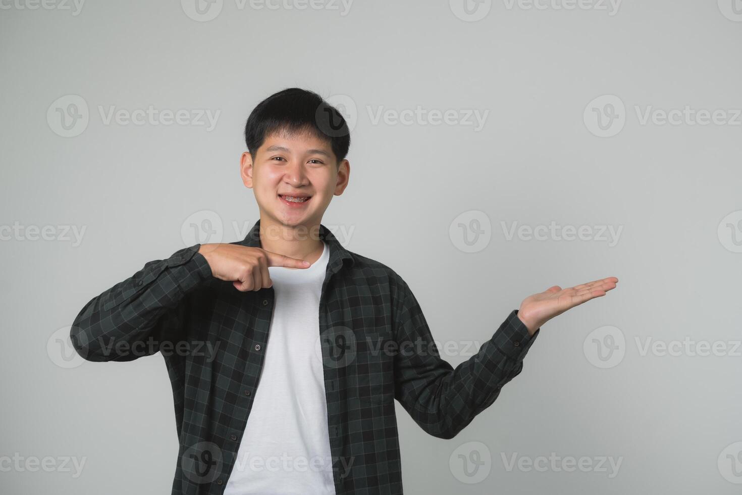 adolescente hombre chico con tirantes presentación con mano gesto. asiático adolescente chico con dental tirantes haciendo un presentación gesto en un llanura antecedentes. retrato hermoso hombre en estudio concepto. foto