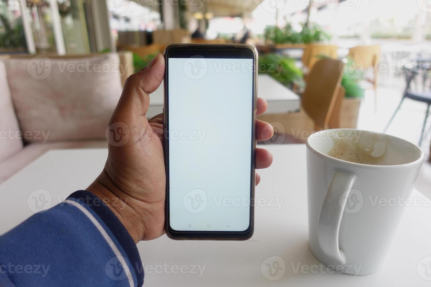 joven hombre mano utilizando inteligente teléfono con vacío pantalla a café foto