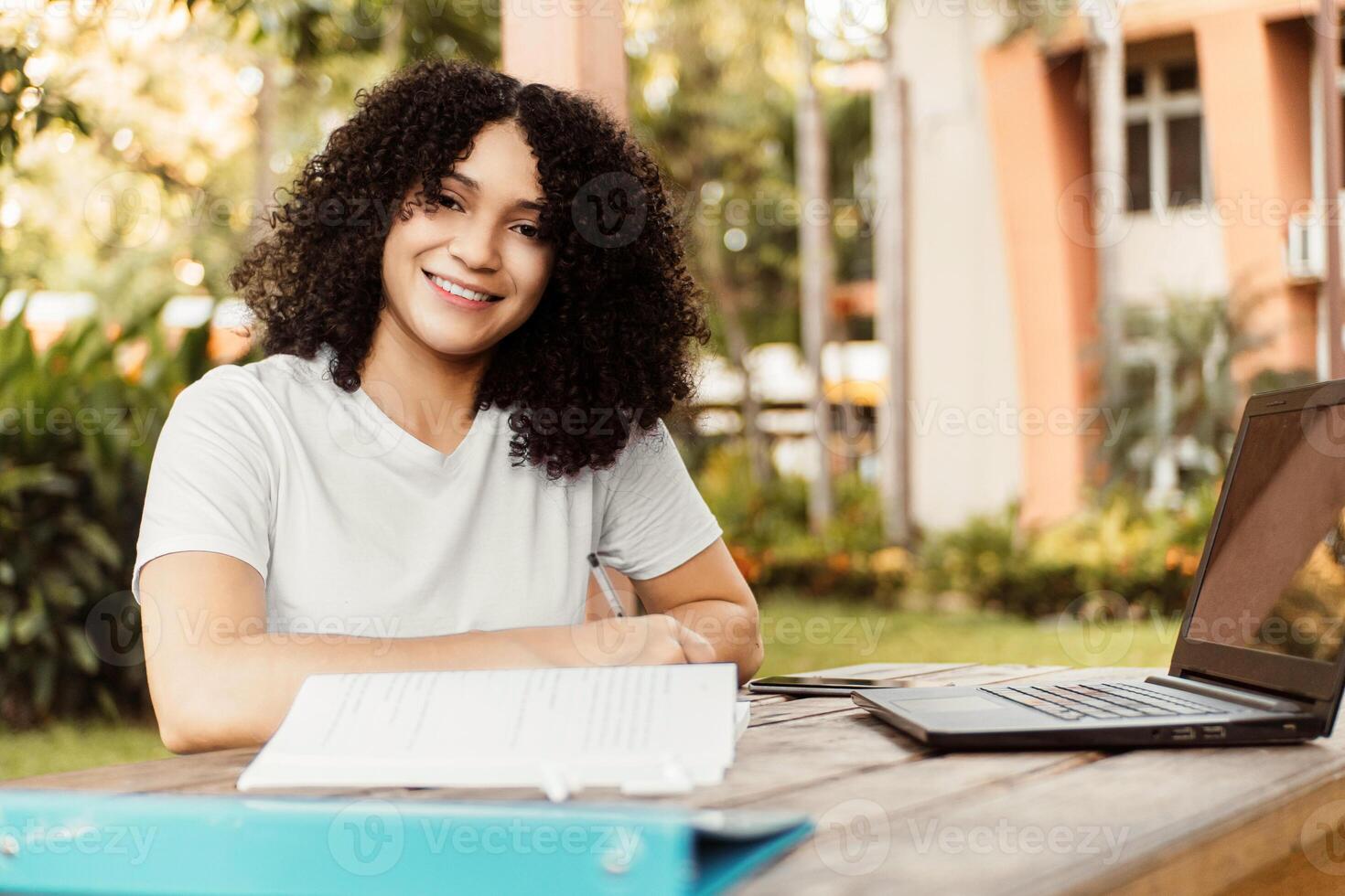 Happy student smiling looking at camera sitting on a chair in a desk at a park. photo