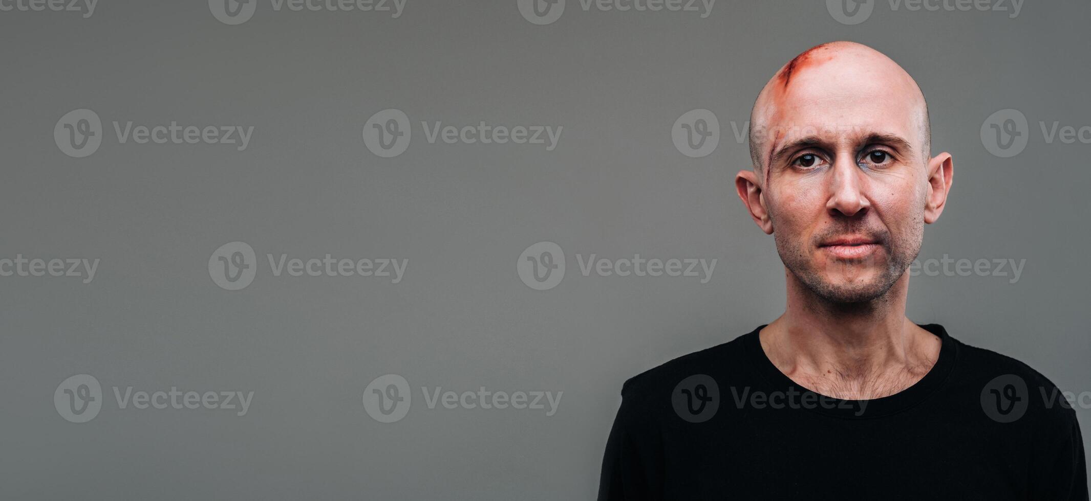 A battered man in a black T shirt who looks like a drug addict and a drunkard stands on a gray background photo