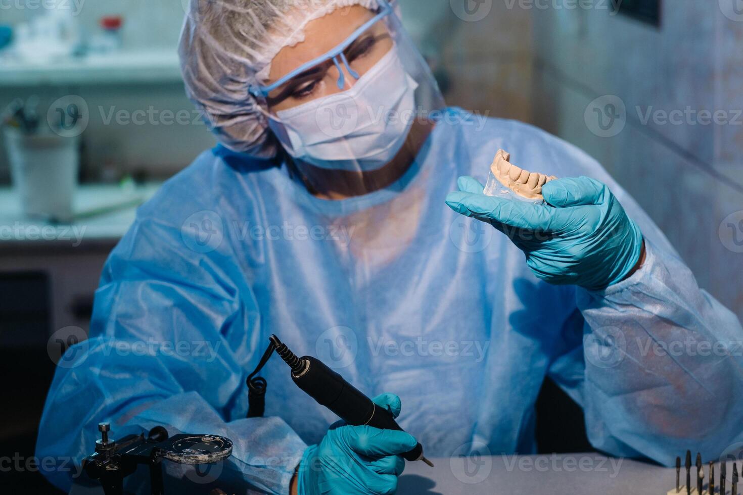 un dental técnico en protector ropa es trabajando en un protésico diente en su laboratorio foto