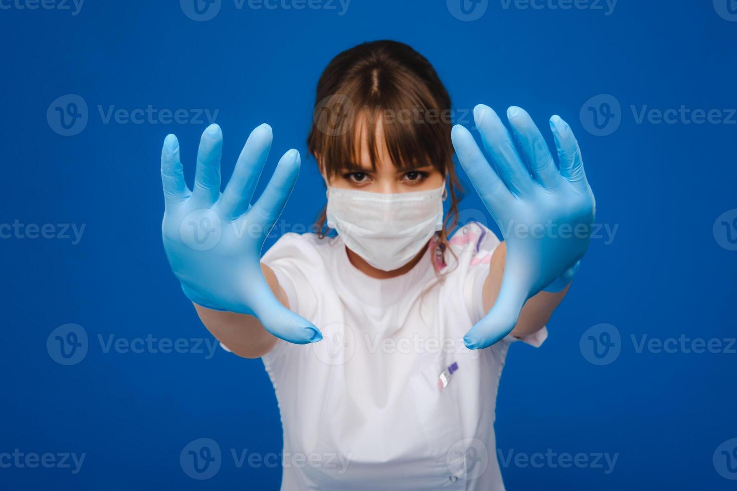 A girl doctor stands in a medical mask and gloves on an isolated blue background photo