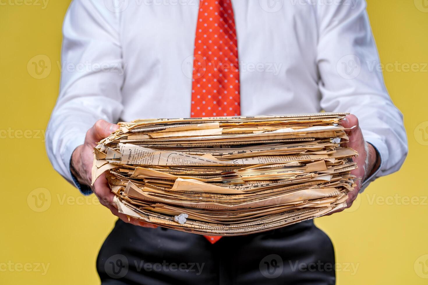 Studio shot of businessman or accountant holding pile of papers. Yellow background photo