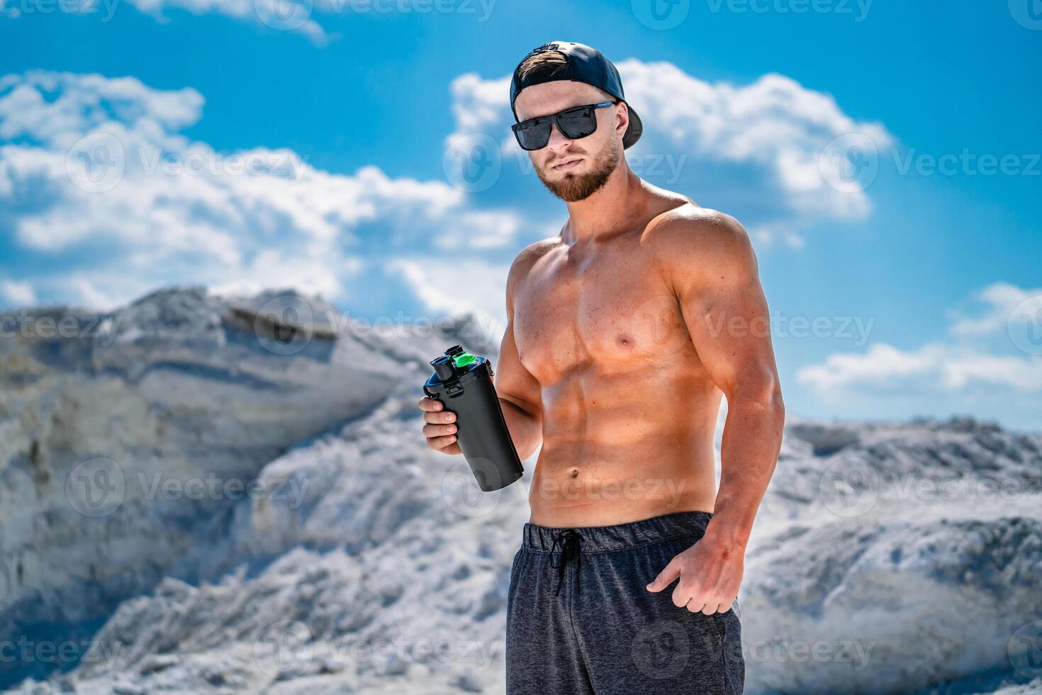 Portrait of a handsome halfnacked bodybuilder man. Glasses and a cap on. Sport bottle of water in hands. photo