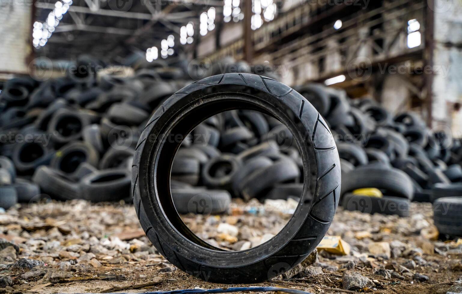 Dirty old tire is on the ground standing next to the other used tyres in the damaged plant. Rubber junk from the car. Close-up photo