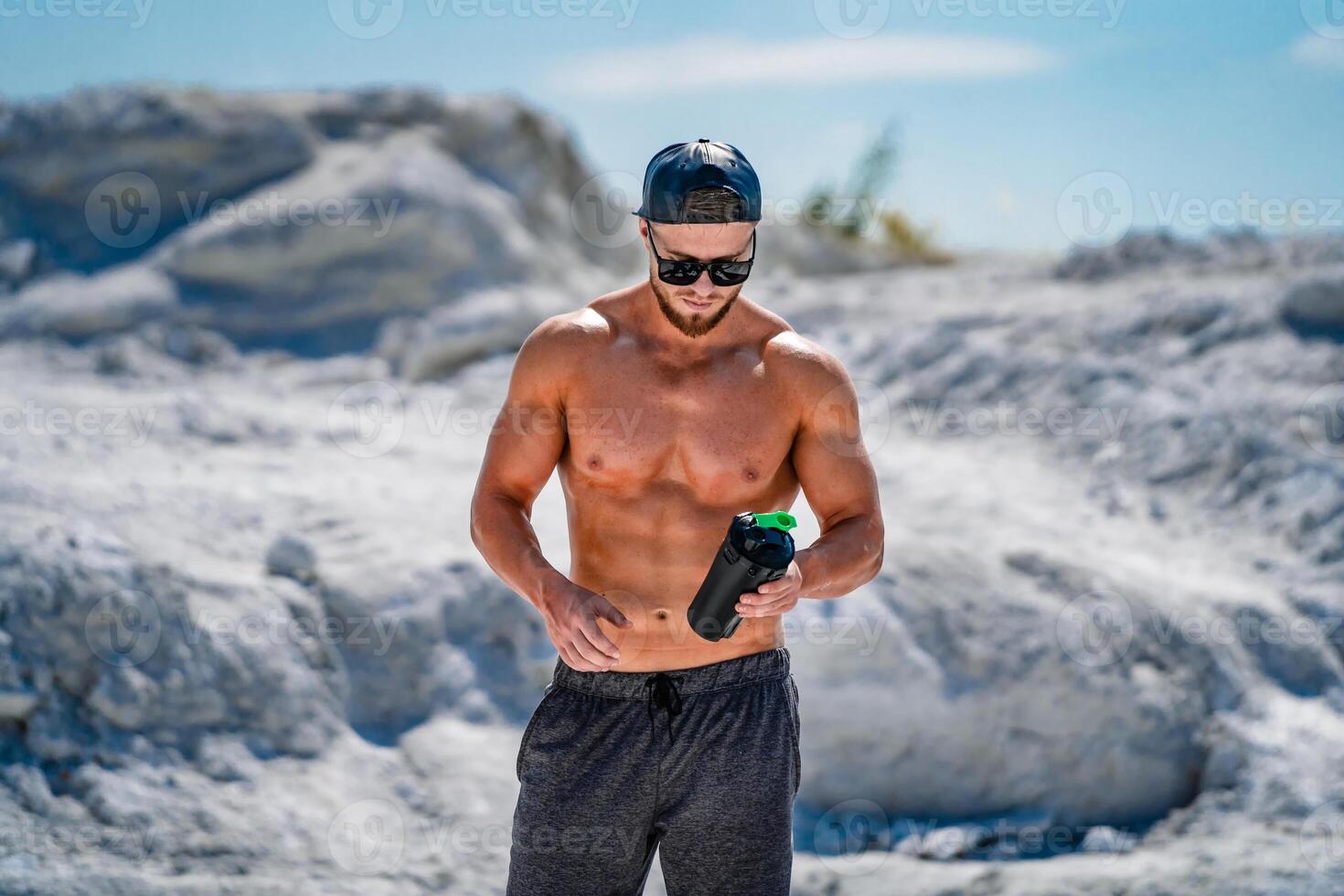 Portrait of a handsome halfnacked bodybuilder man in glasses and a cap with a bottle of water. photo