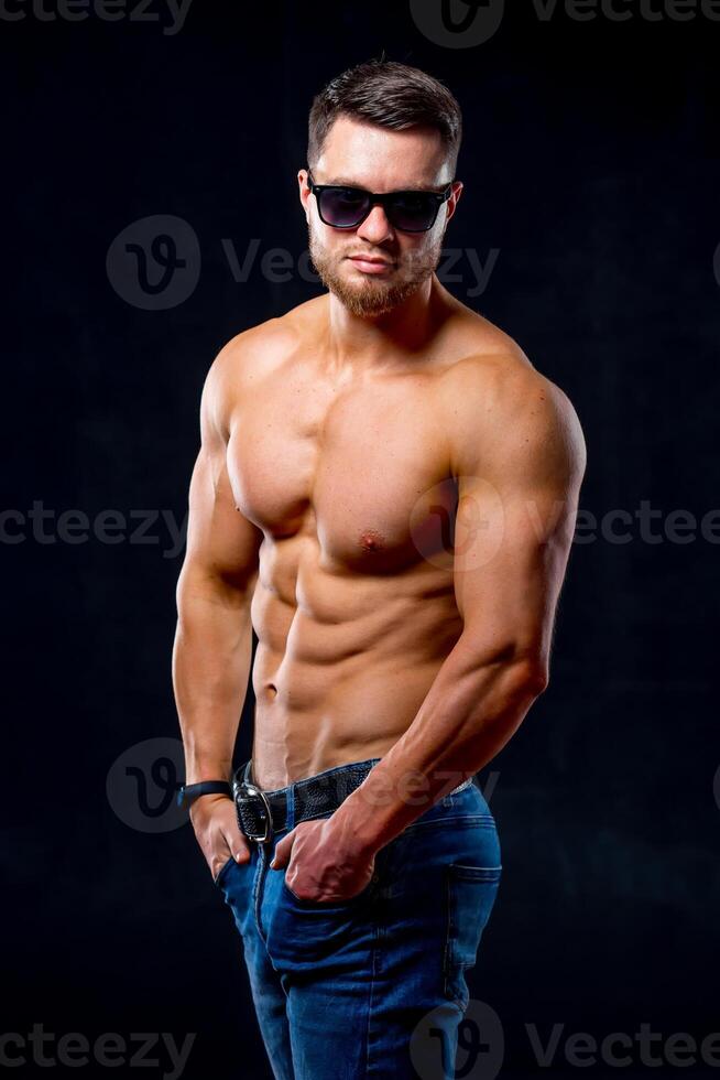 Athletic body. Half turned model guy is posing to the camera in the dark grey background. Studio photo. Strong muscular man. Closeup. photo