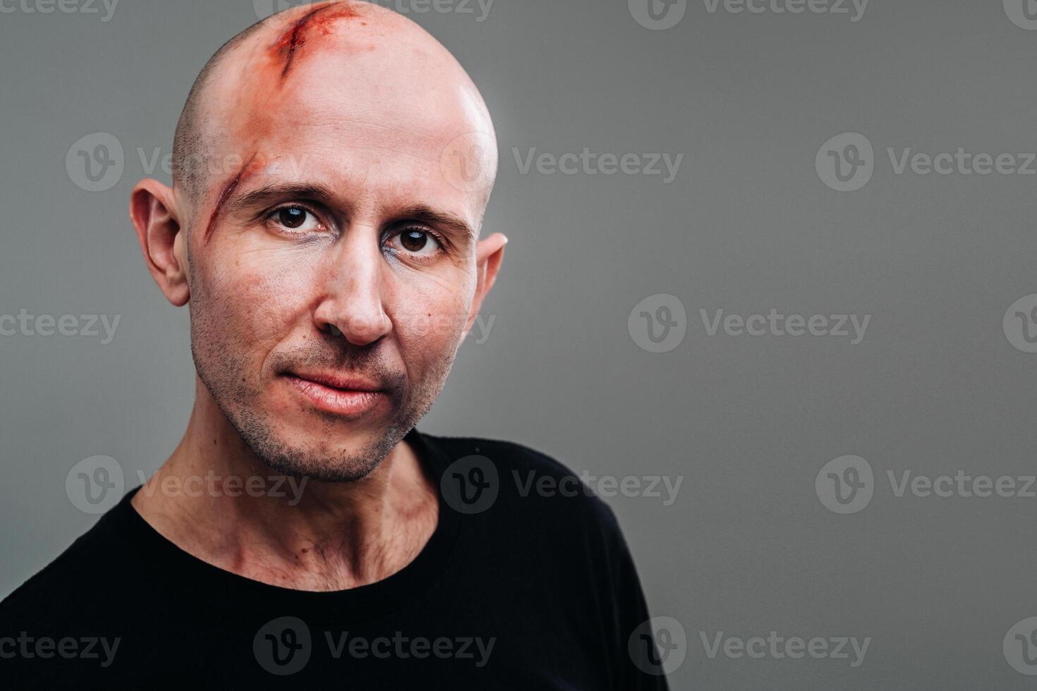 A battered man in a black T shirt who looks like a drug addict and a drunkard stands on a gray background photo