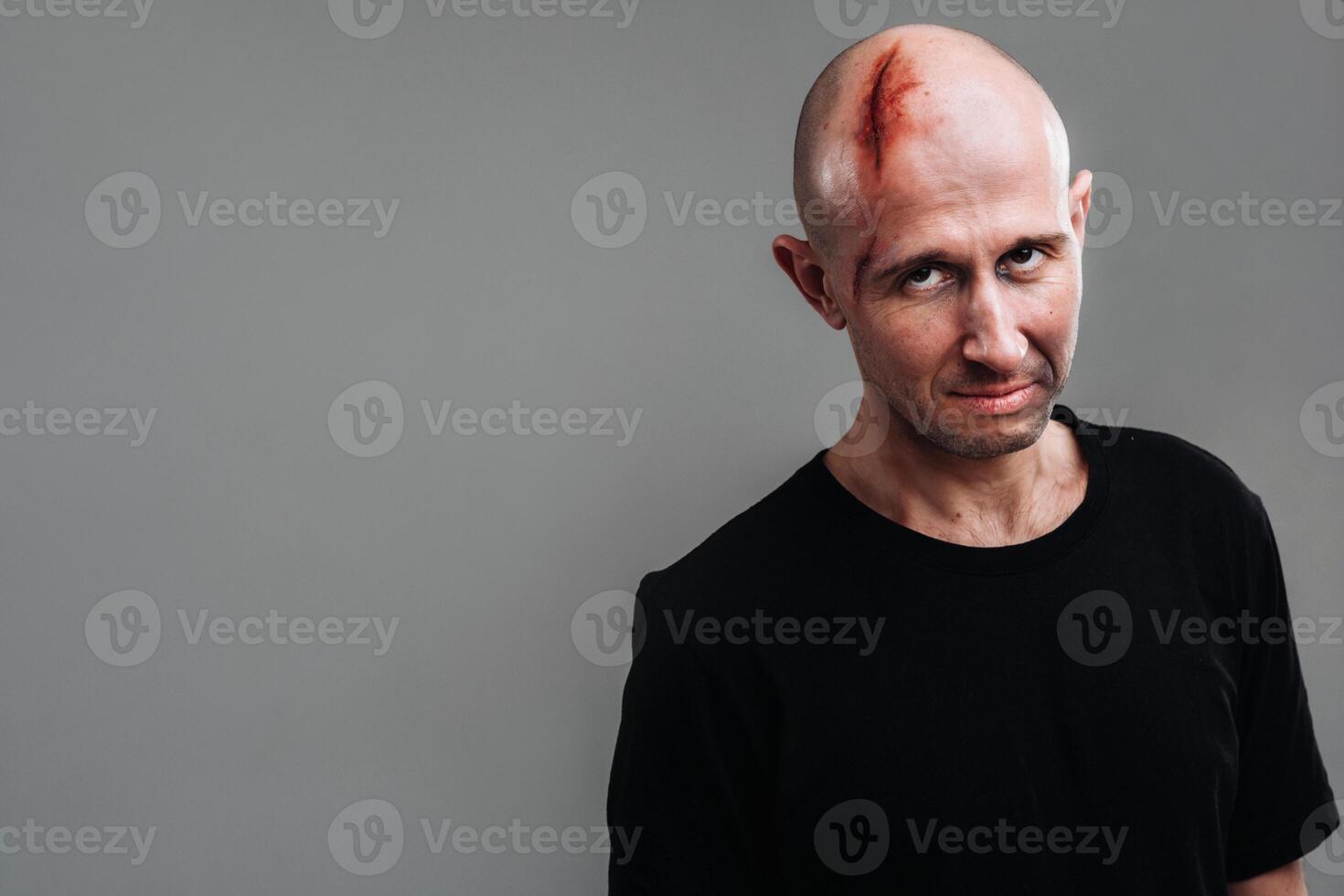 A battered man in a black T shirt who looks like a drug addict and a drunkard stands on a gray background photo