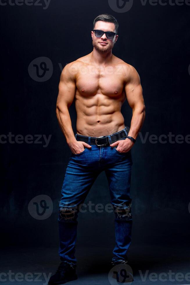 Muscular and fit young bodybuilder fitness male model posing over dark background. Full size photo. photo