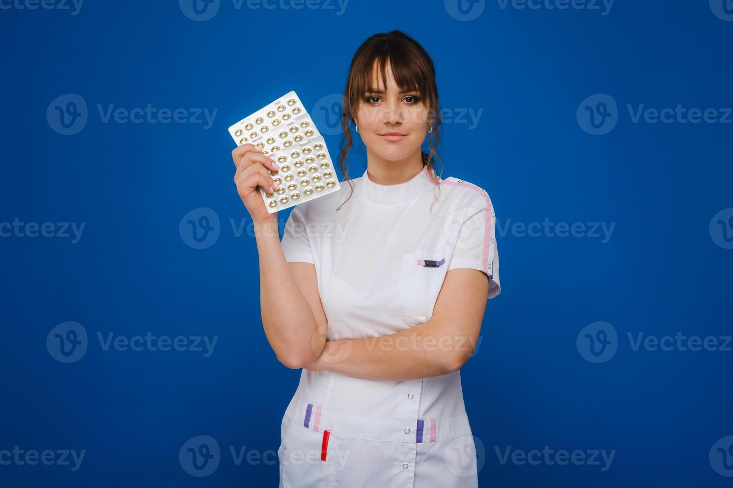 The concept of health care. A young brunette doctor in a white coat on a blue background shows plates with capsules to take. photo