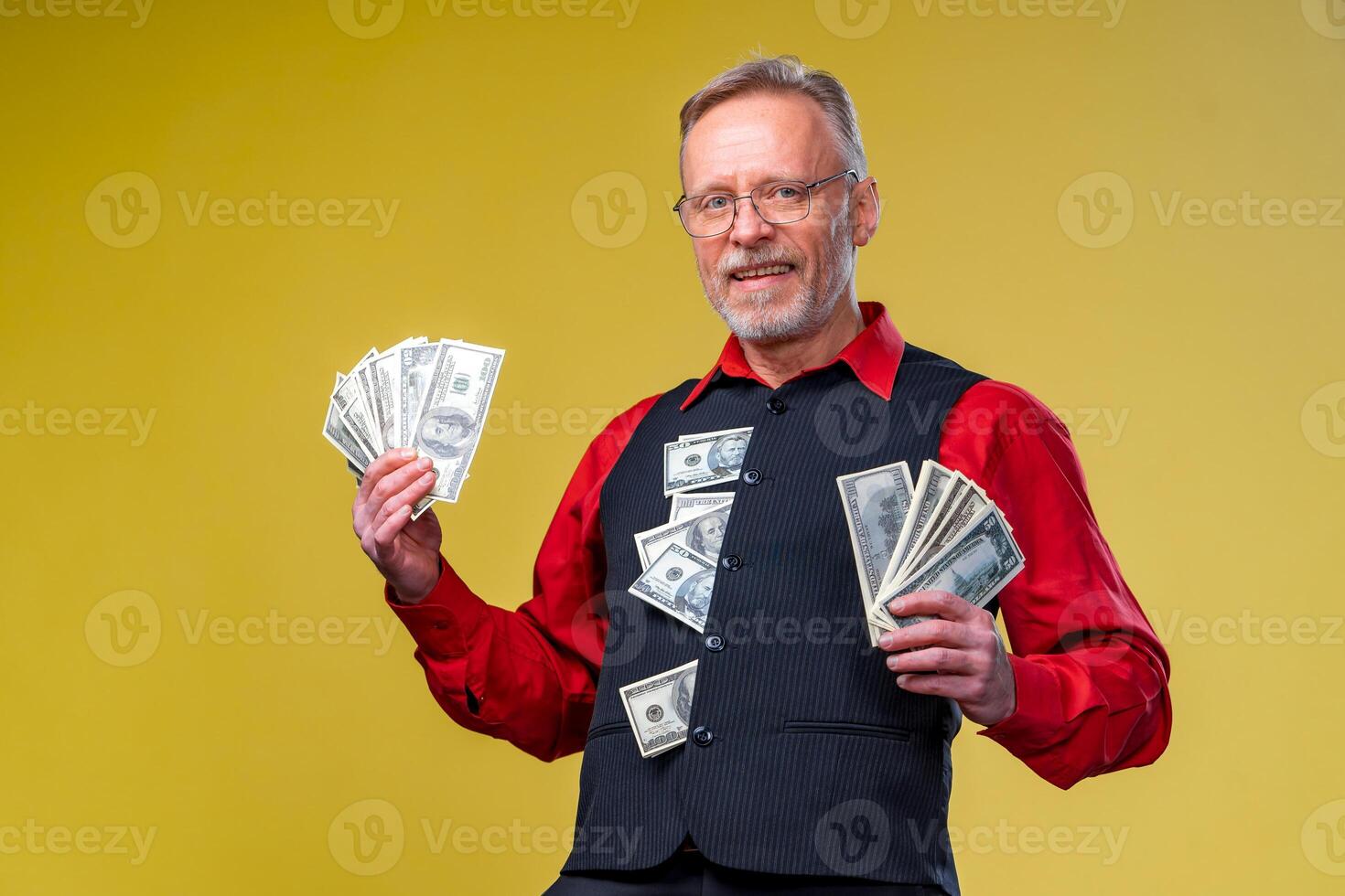 Portrait of happy and white teeth smile senior old business man holding money in hands, dressed in red shirt, isolated on yellow background. Human emotions and facial expressions photo