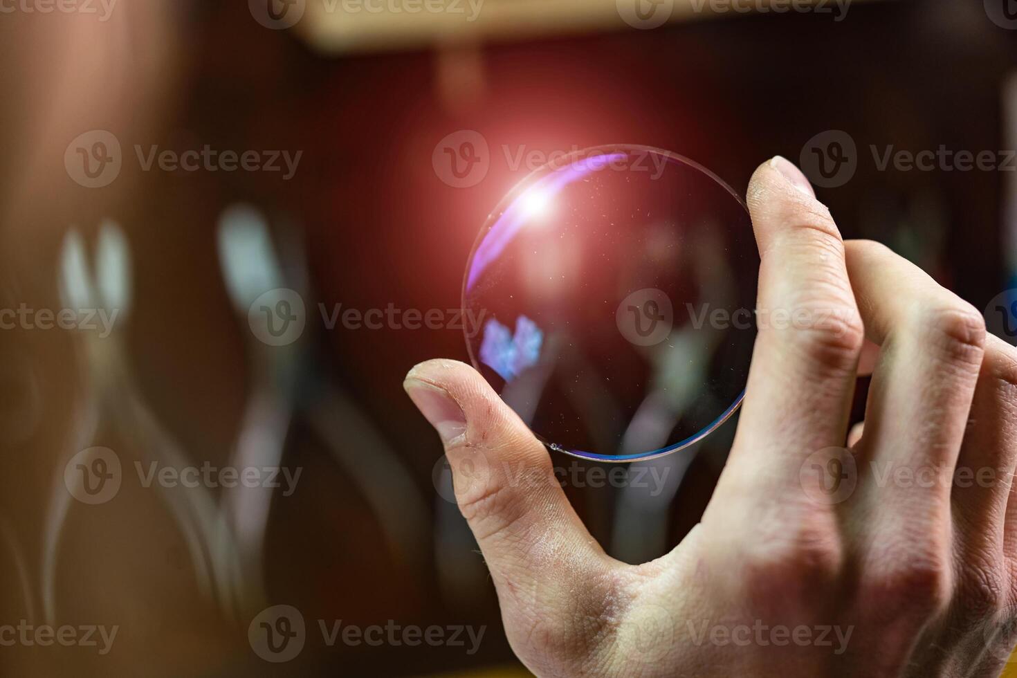 ophthalmologist hands showing a glass lens for spectacles. Blurred background. Ophtalmologist equipment. Vision correction concept. Closeup photo