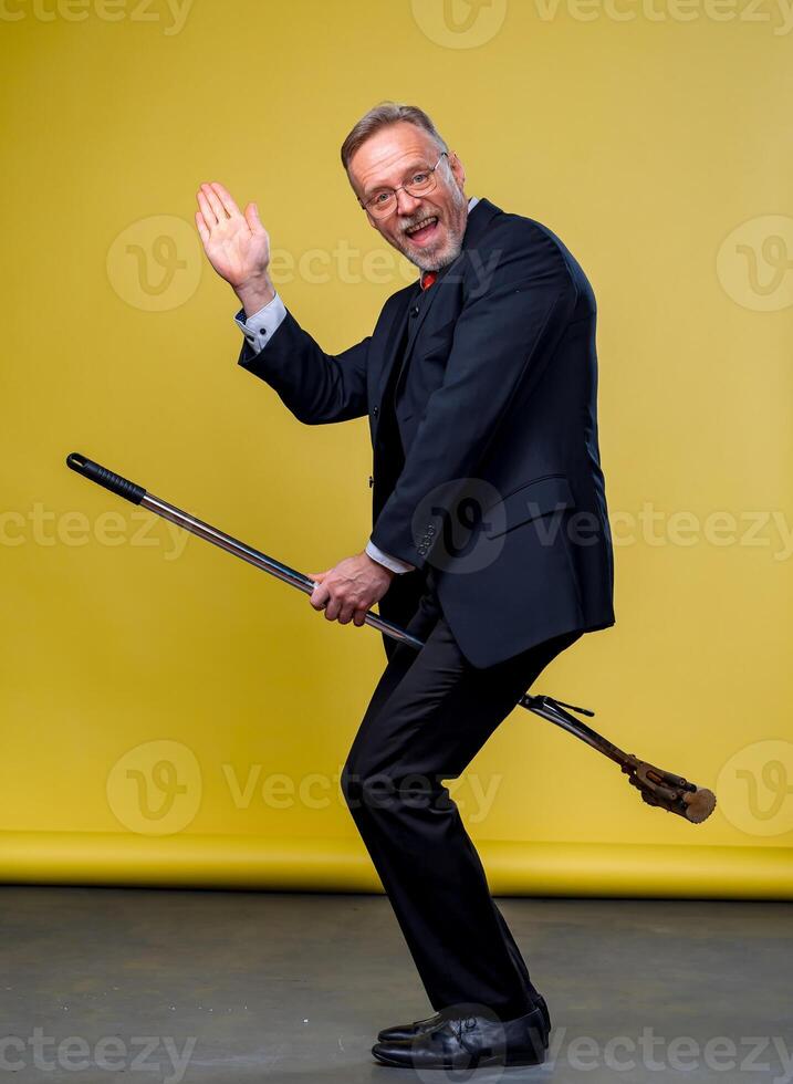 Senior man in suit sitting on a boom. Manager man playing funny games with a mop in studio. photo