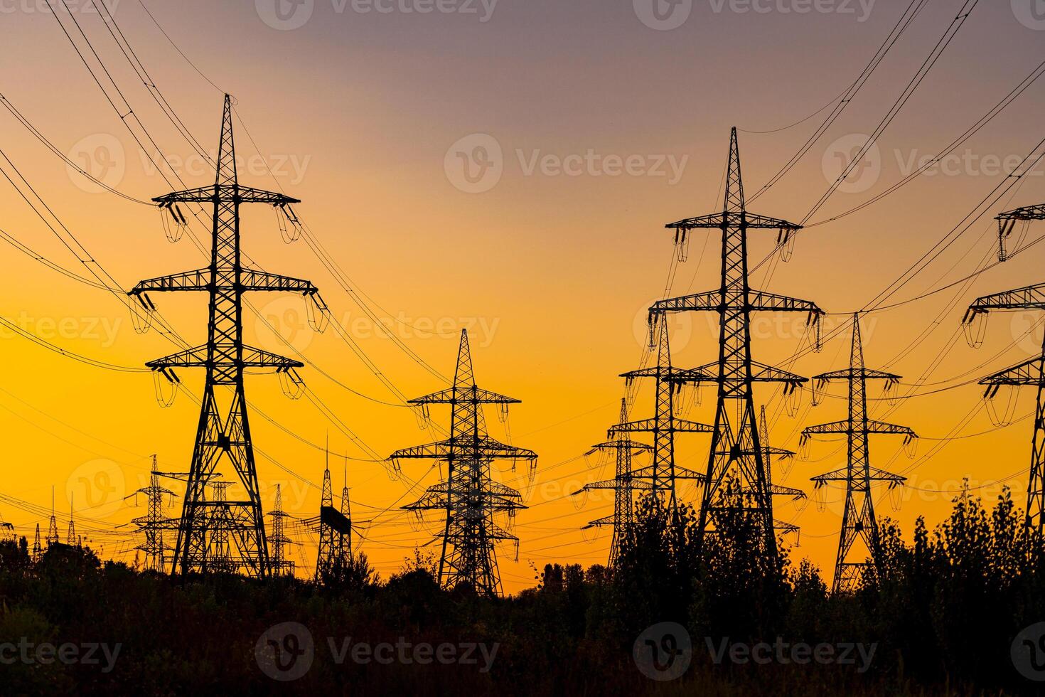 Power pylons on sunset time background. Electricity pylons and high-voltage power lines on the high trees silhouettes. photo