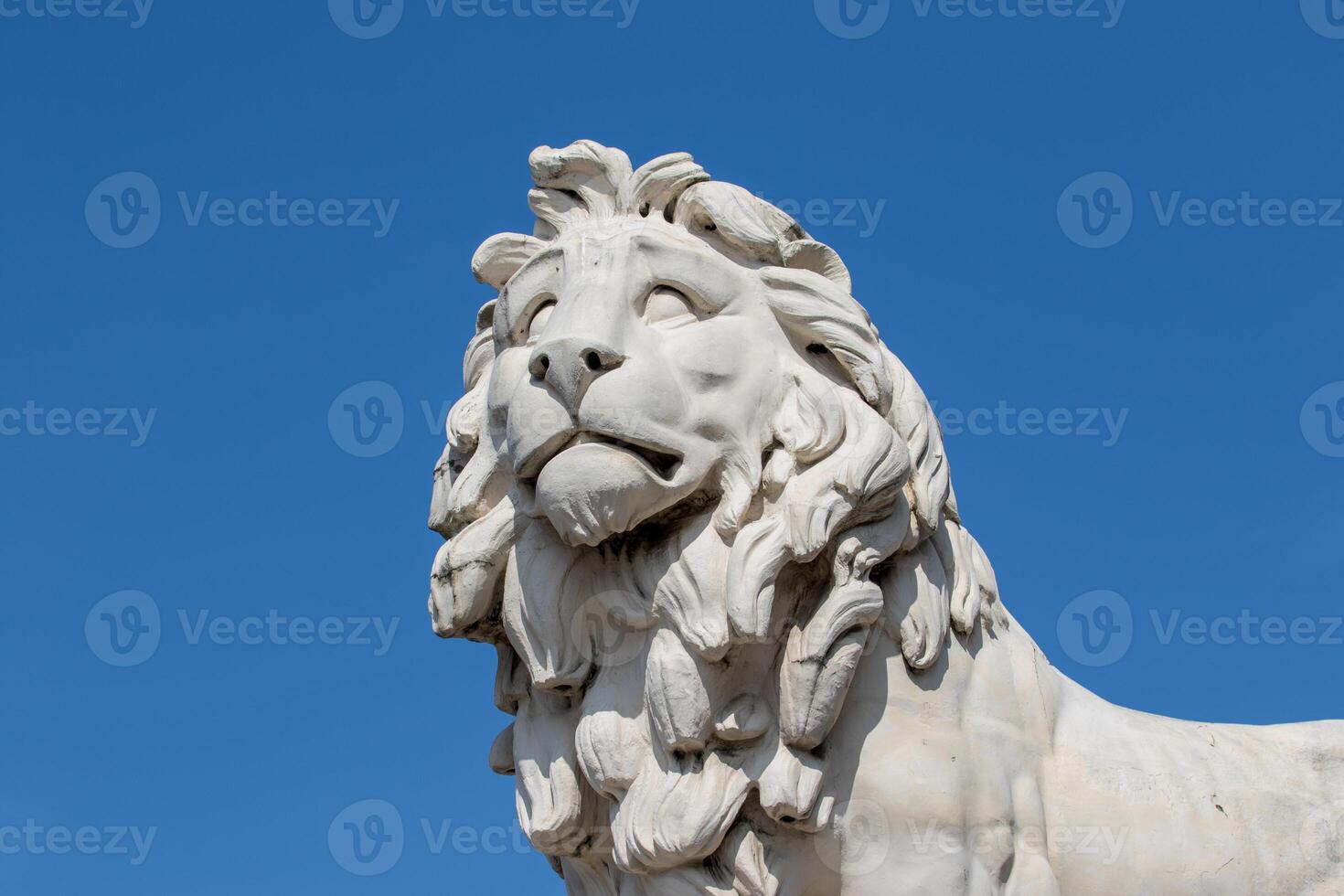 Marble lion statue against a clear blue sky, showcasing intricate details and craftsmanship. photo
