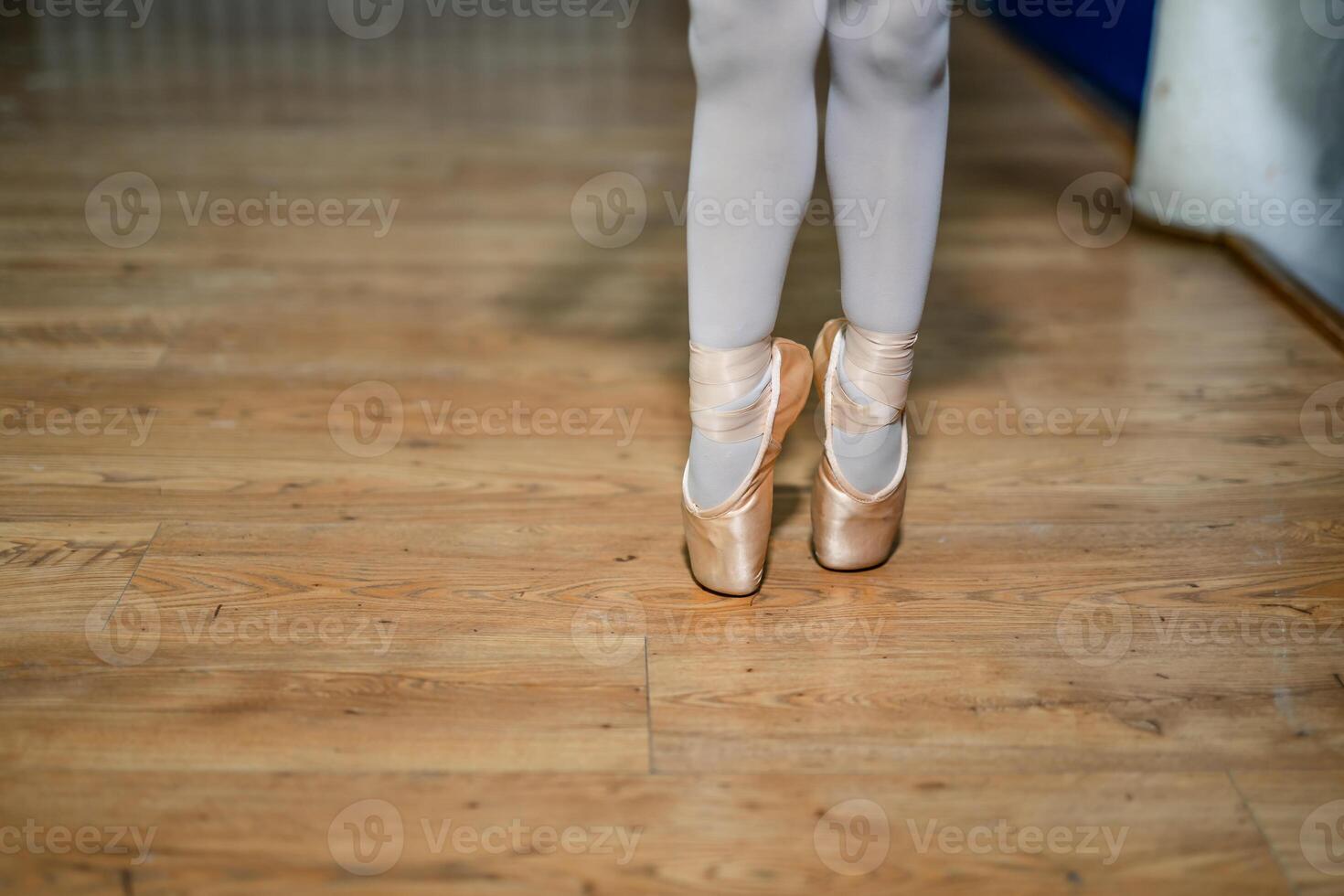 Legs of a little ballerina in a gold ballet shoes and white socks posing tiptoe in ballet hall on the floor. Closeup. photo