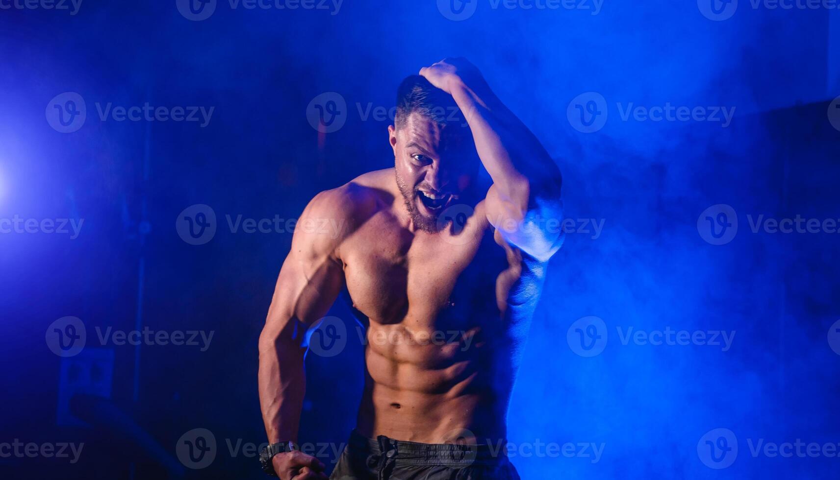Athletic body. Half turned model guy is posing to the camera in the dark blue light background. Strong muscular man. Closeup. photo