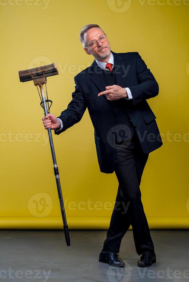 Senior man in suit holding a boom. Manager man pointing at mop in studio. photo