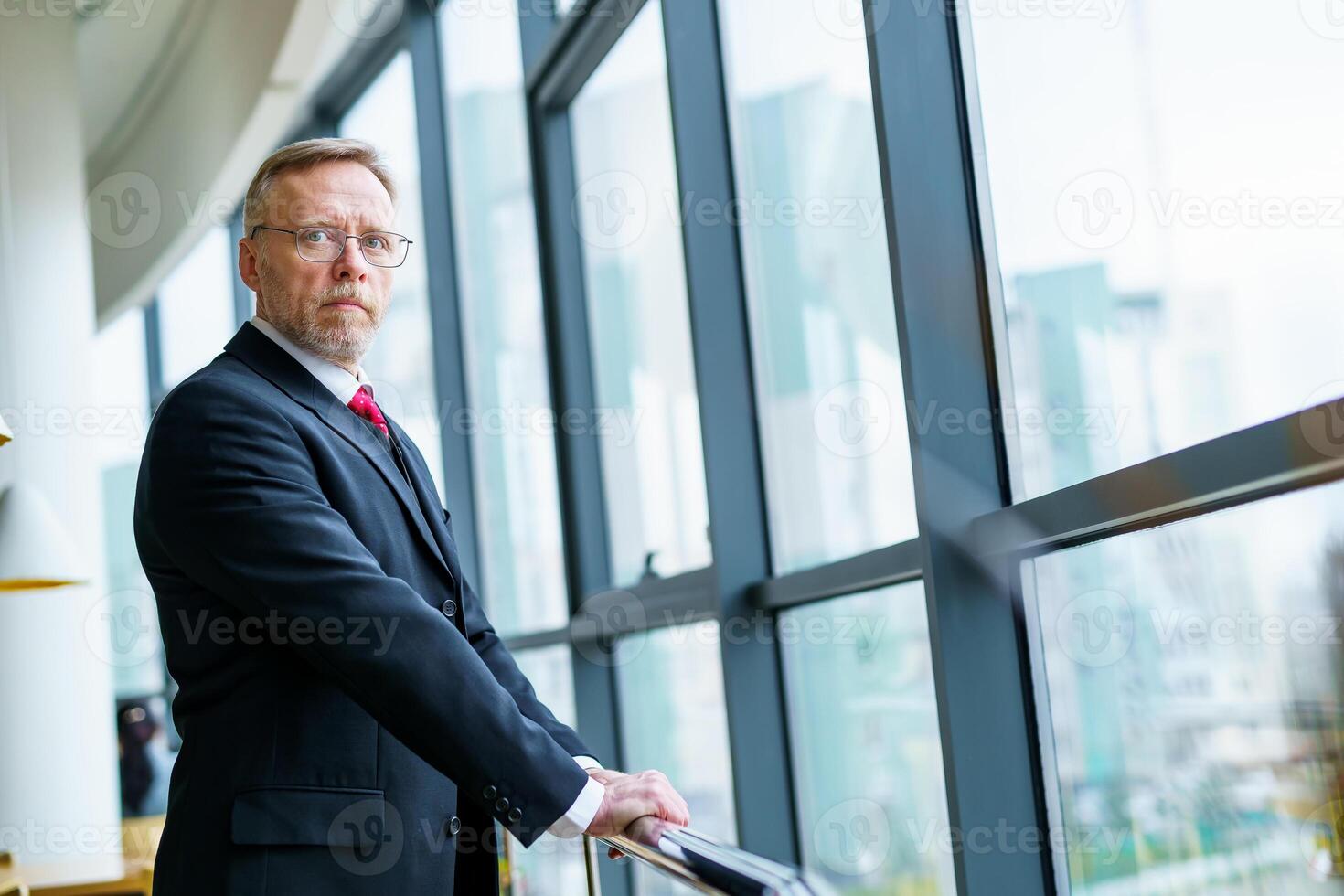 Portrait of a senior businessman standing against big windows background. Modern suit, photo