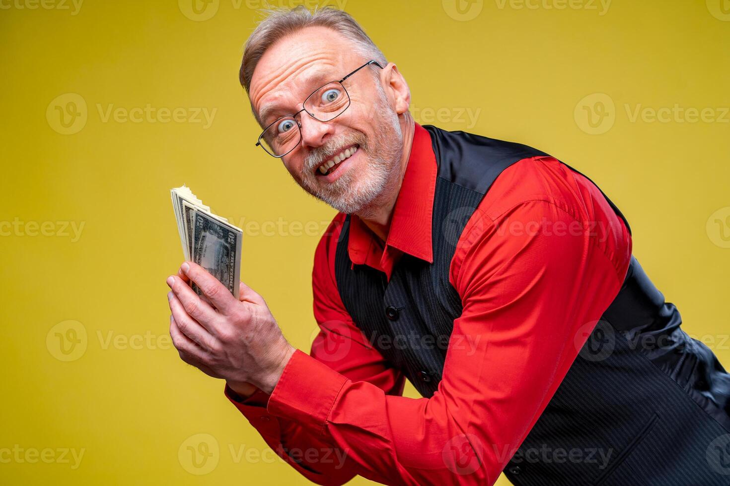 Portrait of super excited senior mature man who just won lots of money, trying to give money to the camera, isolated on yellow background. Positive emotion facial expression feelings. Closeup photo