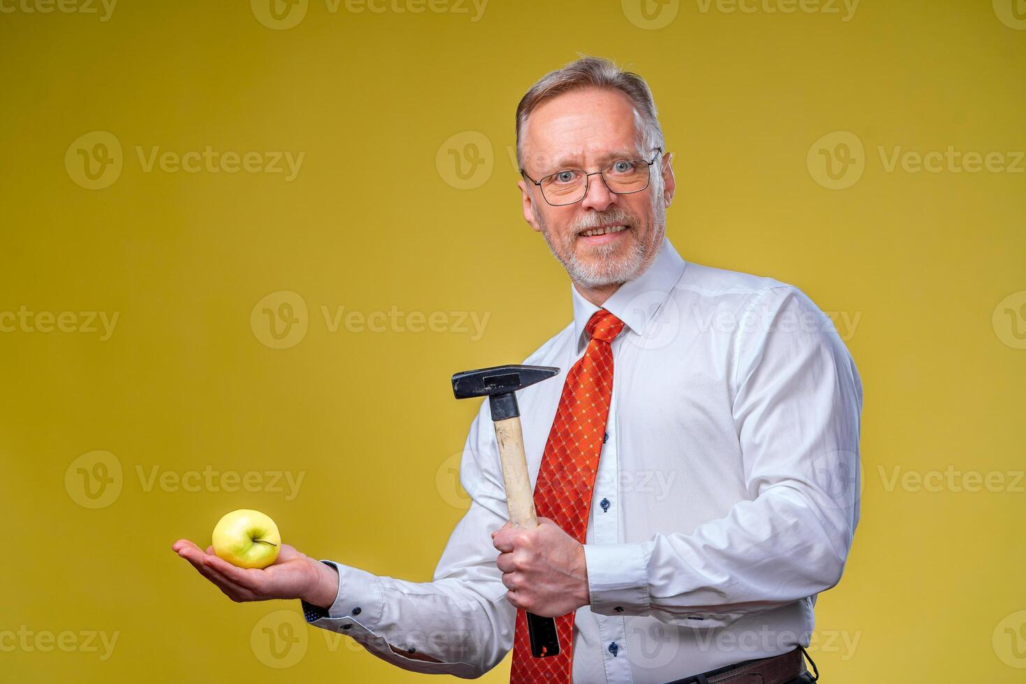 Senior business man wearing shirt. Man with hammer and an apple. Isolated on yellow background. Side view. photo