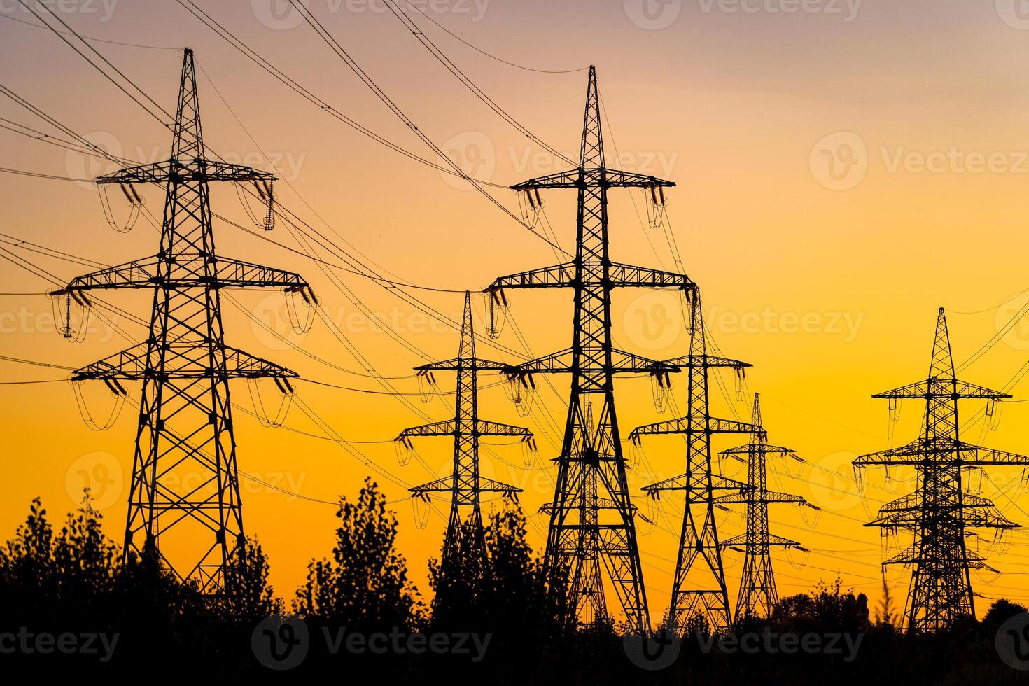 Power pylons reache into the sunset sky. Silhouettes of big trees under energy transmission towers. photo