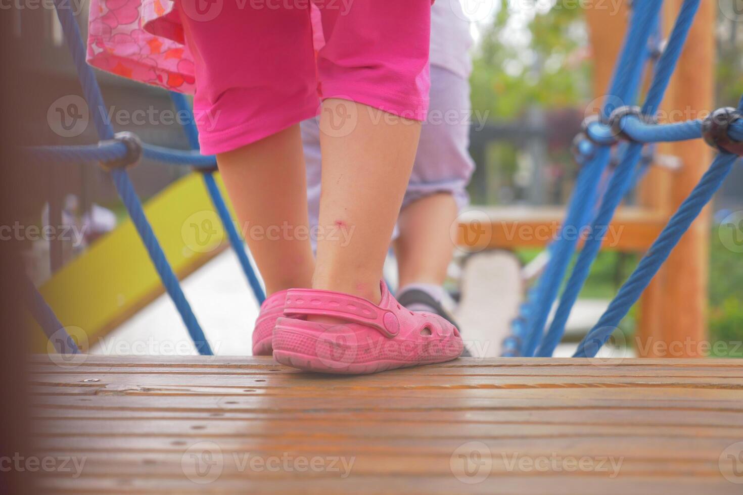 A little girl in pink shoes is standing on a wooden deck photo