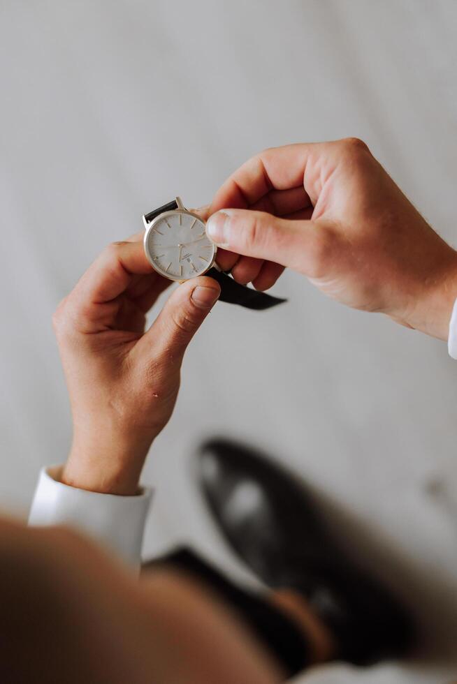 A close-up of a cropped frame of a man puts on a watch with a leather belt, is dressed in a stylish suit, a white shirt, wears a gold ring. photo