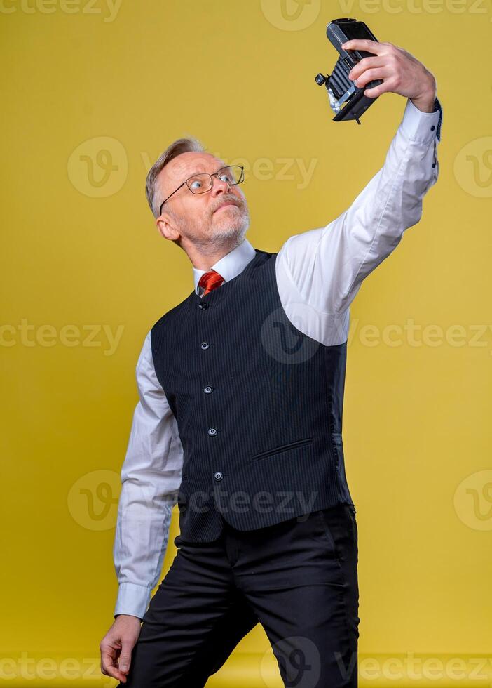 Cheerful elderly gray-haired mustache bearded man in shirt isolated on yellow background. People lifestyle concept. Doing selfie shot on mobile phone from above photo