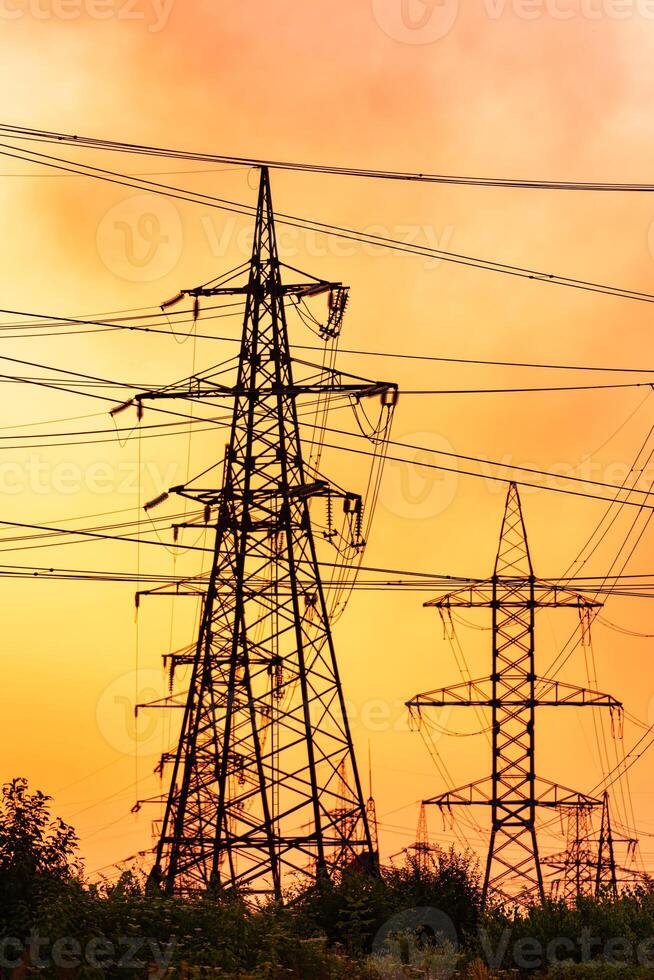 Tower of power lines on a background of orange sky. Transmission power, power tower on an empty farm land at the sunset photo