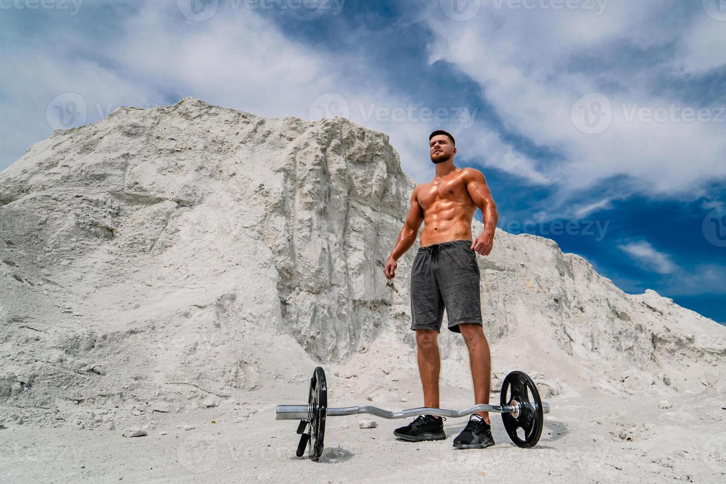 Handsome strong man showing his muscles advertising active sport healthy lifestyle. Bodybuilder posing outdoors. Photoshoot in a quarry. photo