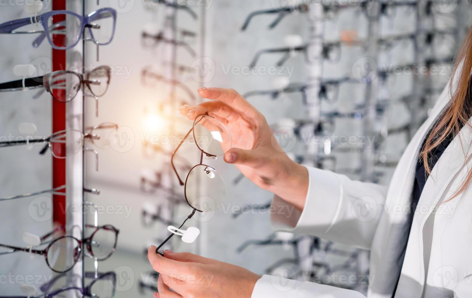 Showcase with spectacles in modern ophthalmic store. Hands with glasses. Closeup. photo